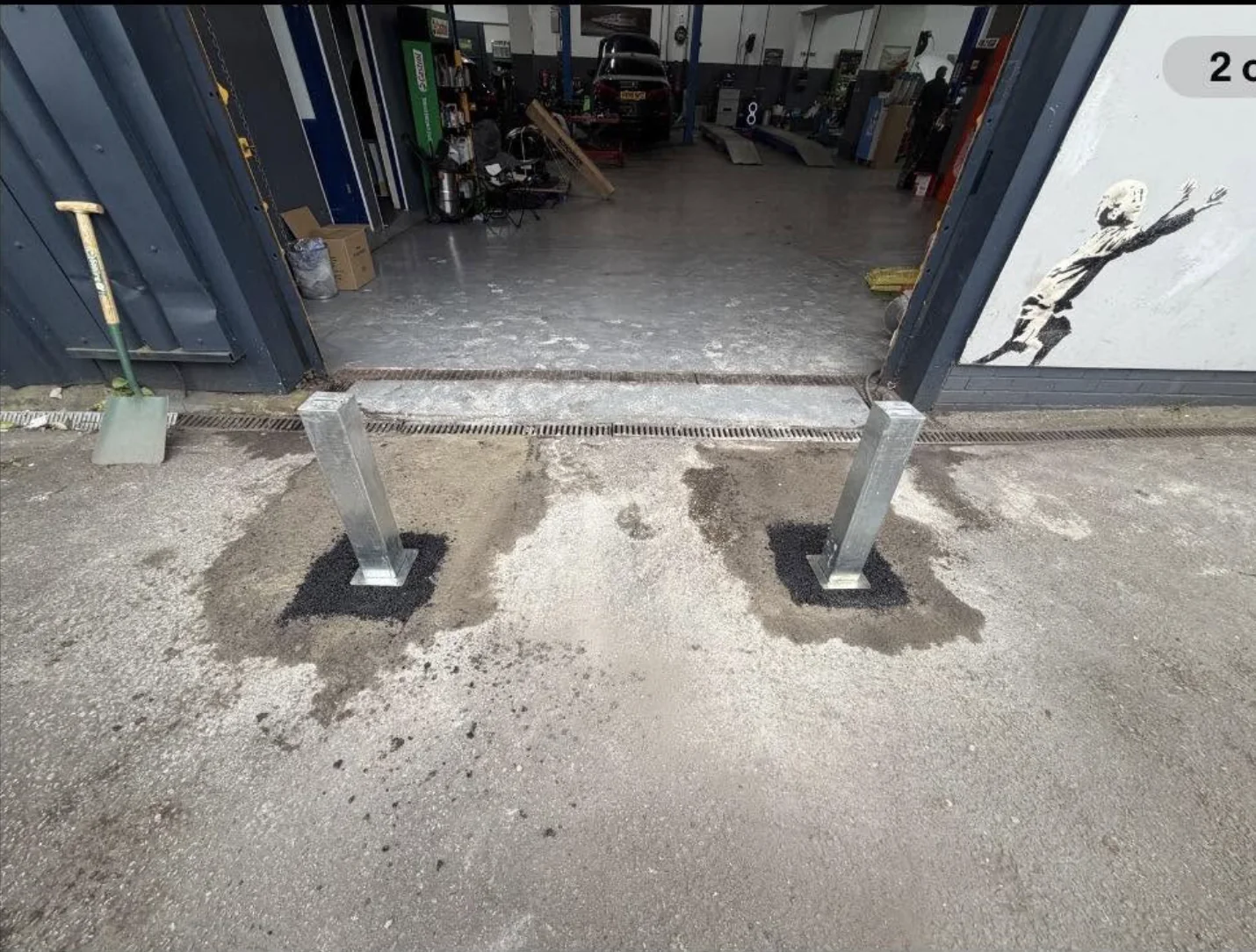 Two galvanised POSTSECURE telescopic posts installed across a workshop entrance