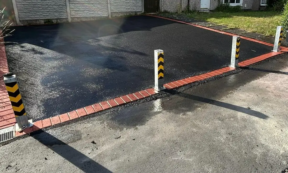 Black and yellow chevron-marked telescopic security posts installed along a newly surfaced tarmac driveway entrance